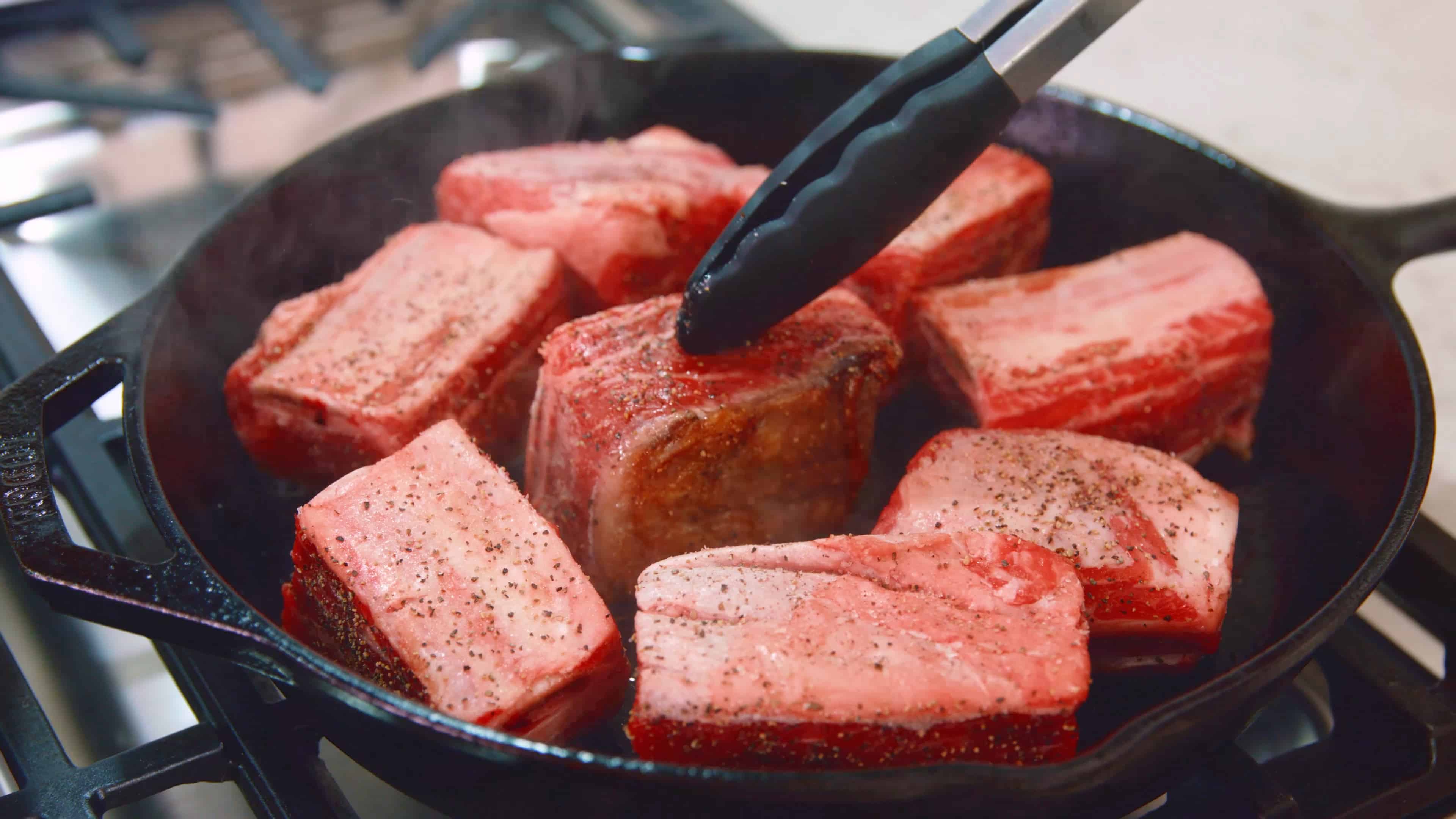 Beef short ribs getting seared in a cast-iron skillet. 
