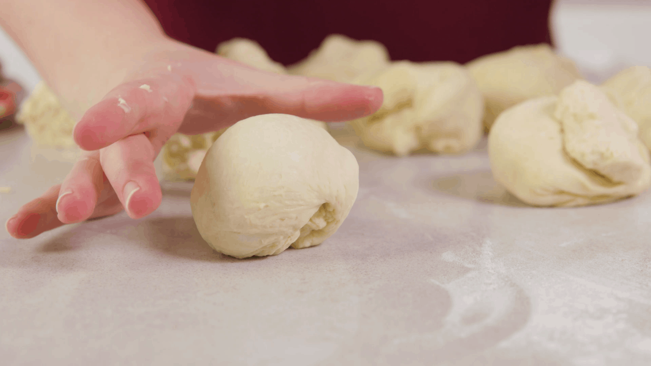 Hand in cupping shape ready to shape dough into balls on a clean countertop.