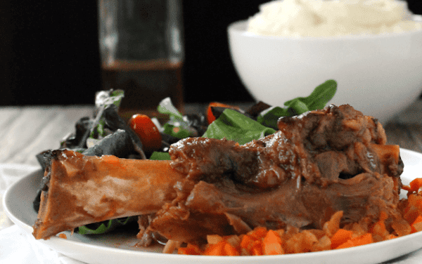 Slow cooker citurs lamb shanks on a white plate witha salad.