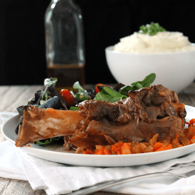Slow cooker citurs lamb shanks on a white plate witha salad.