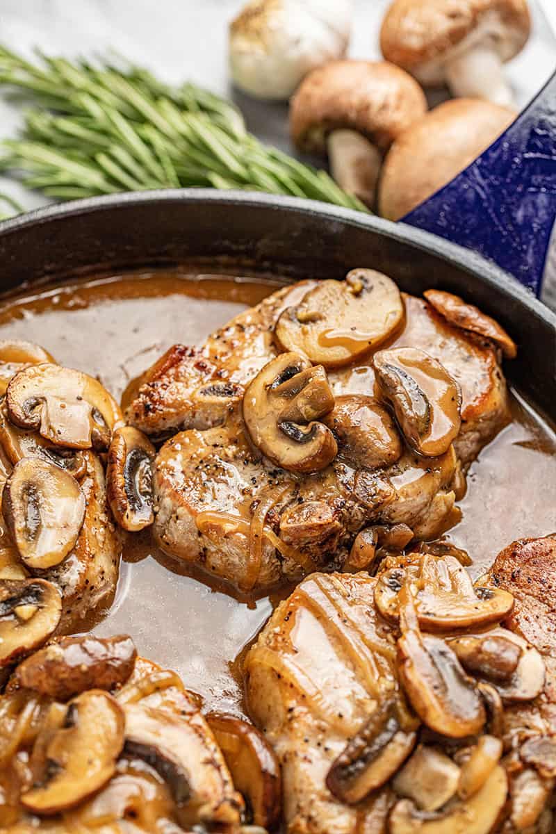 Smothered Pork Chops covered in mushrooms in a cast-iron skillet.