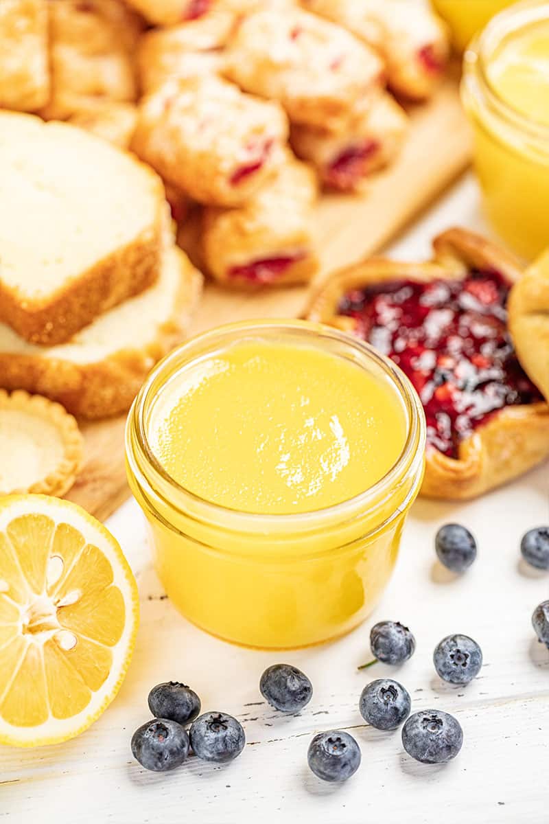 Lemon curd on a white countertop surrounded by desserts and fruit.