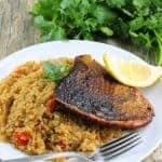 Blackened salmon portion over quinoa on a white plate with a lemon wedge