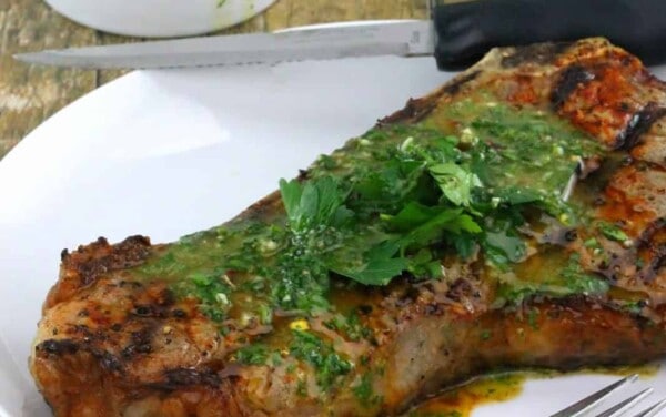 Steak with Chimichurri all over it on a white plate.