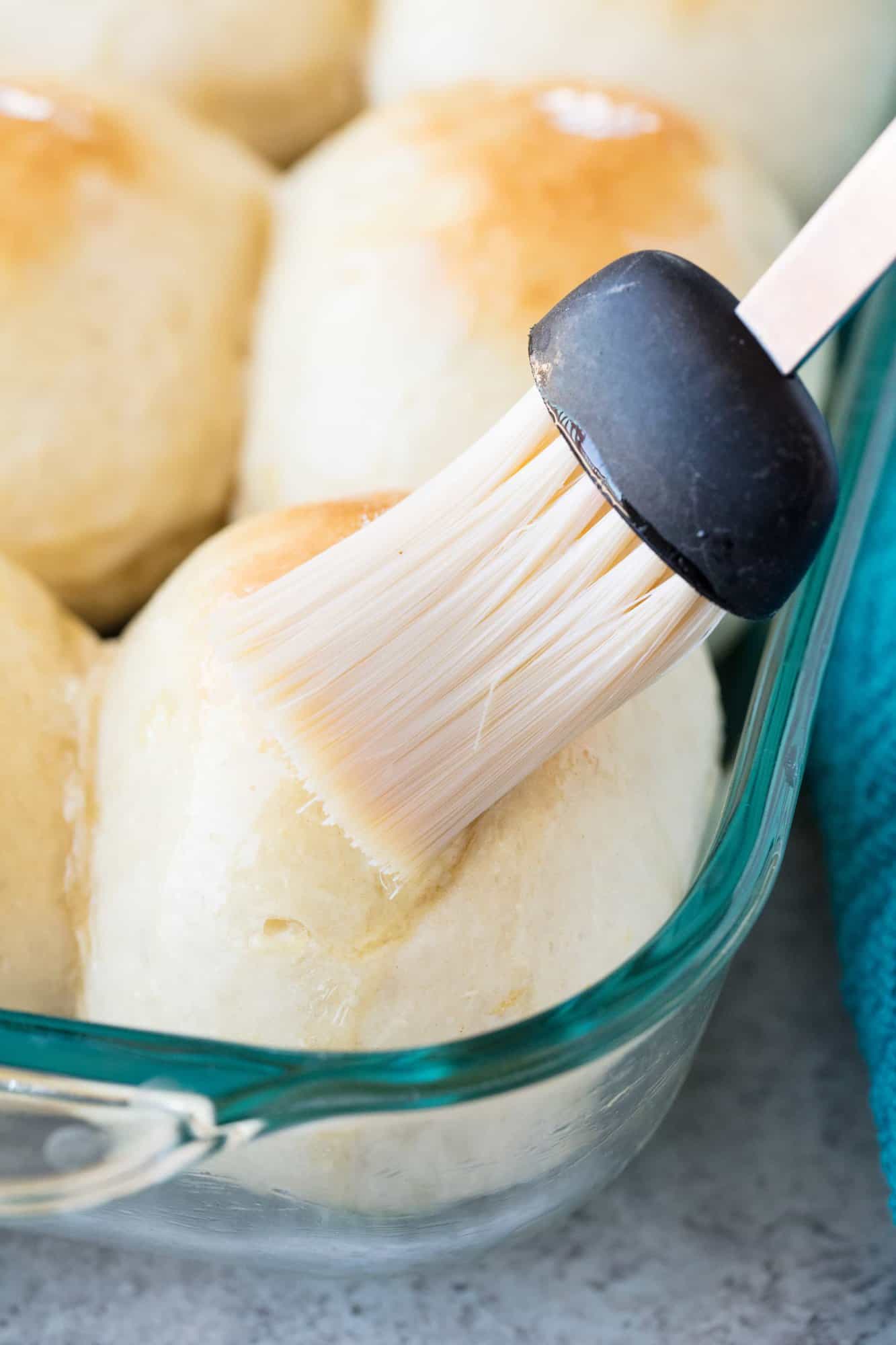 Butter is brushed onto a pan of Homemade Hawaiian Sweet Rolls