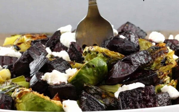 Beets and brussel sprouts topped with goast cheese in a white bowl with a fork in the middle of it.