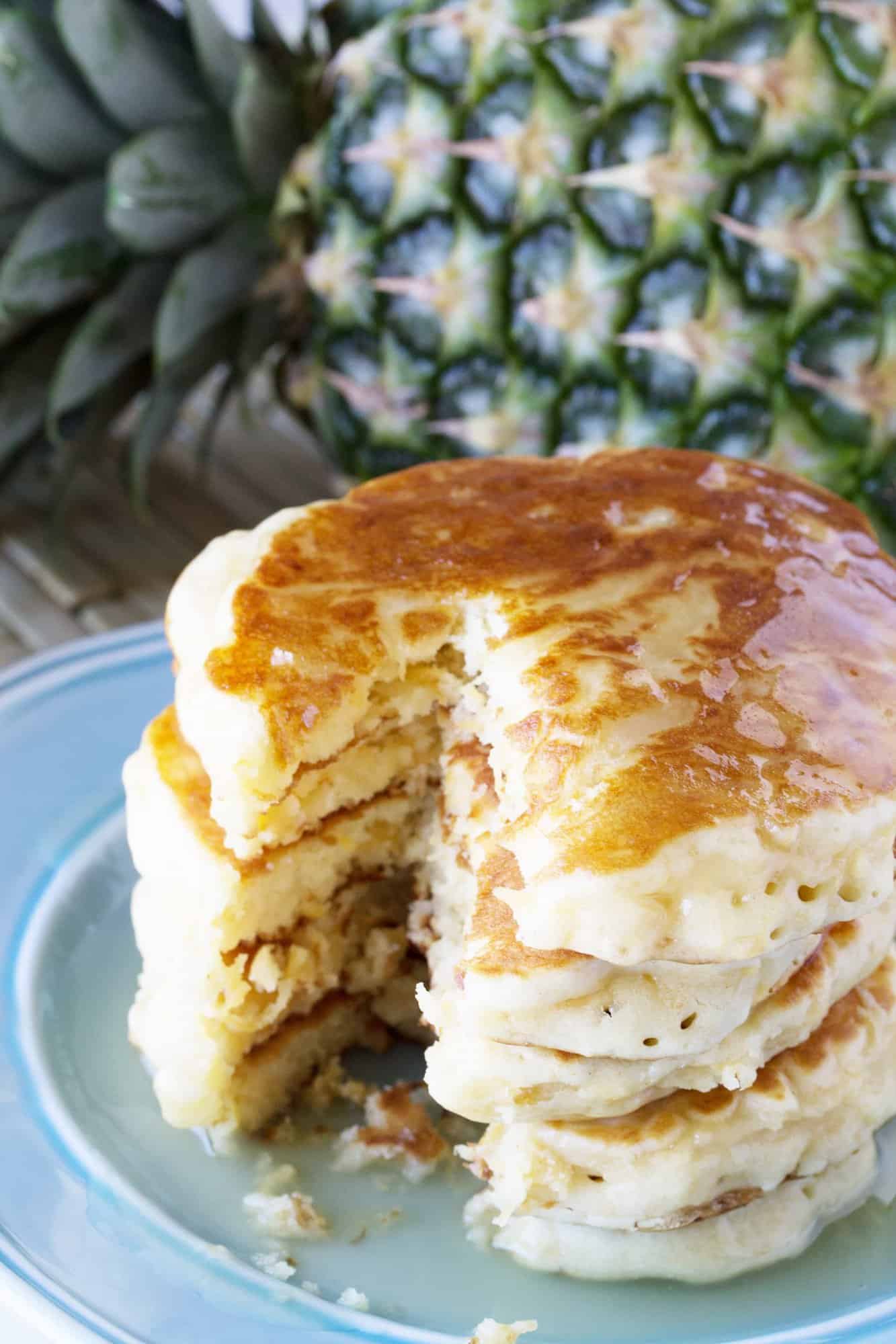 Pineapple Pancakes with Coconut Syrup over them with a bite cut out of the stack.