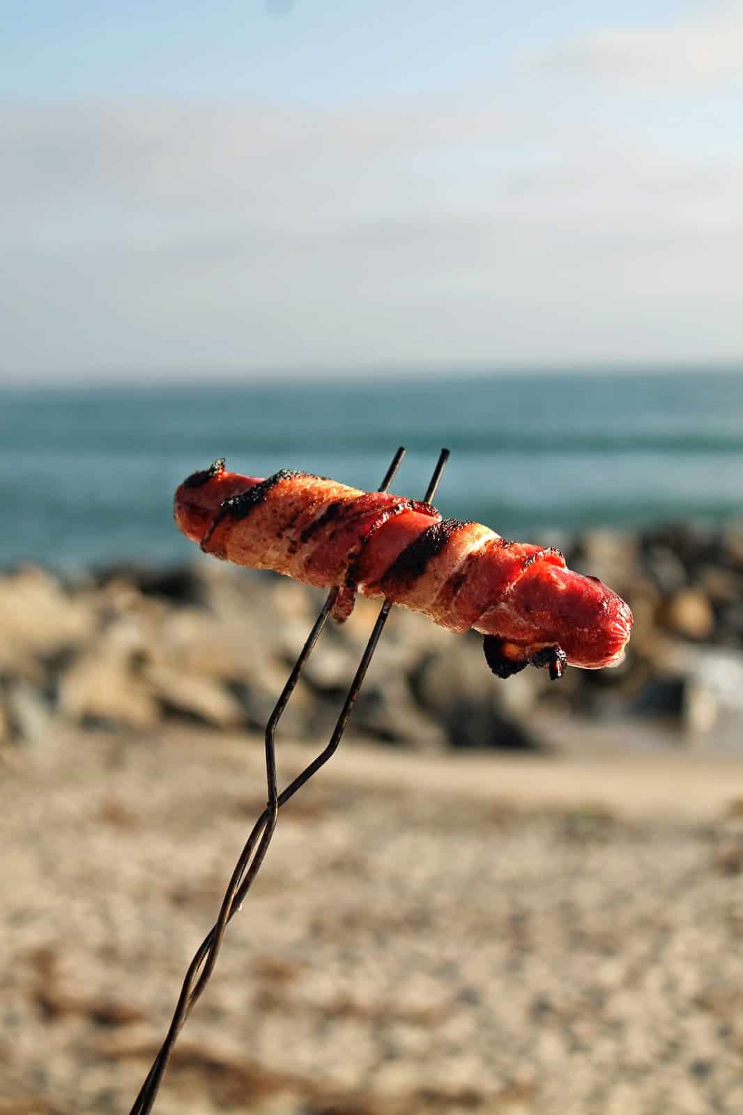 Campfire cooked bacon wrapped hot dog on a skewer 