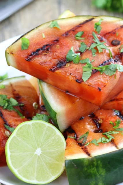 Close up of A stack of cilantro lime grilled watermelon on a white plate with half a lime.