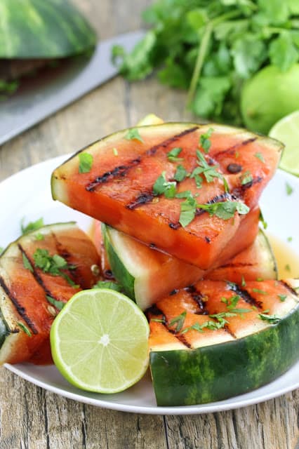 A stack of cilantro lime grilled watermelon on a white plate with half a lime.
