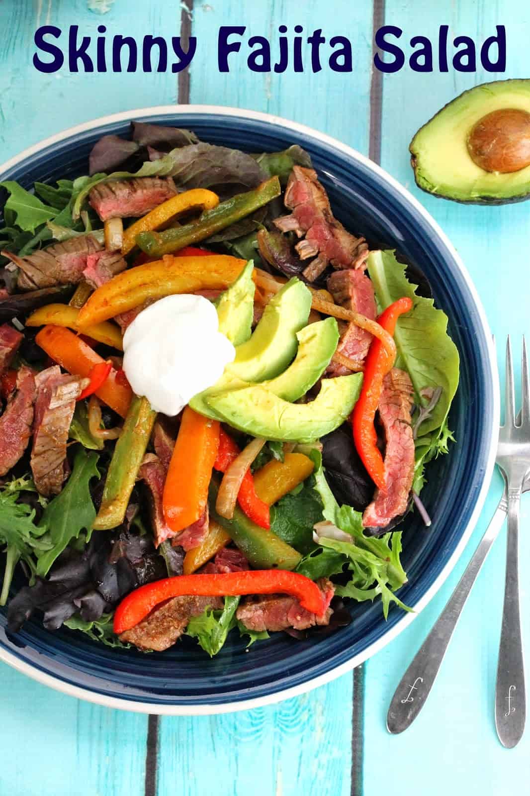Skinny Fajita Salad served up with grilled flank steak, fresh avocado and bell peppers over a bed of lettuce and topped with a dollop of sour cream