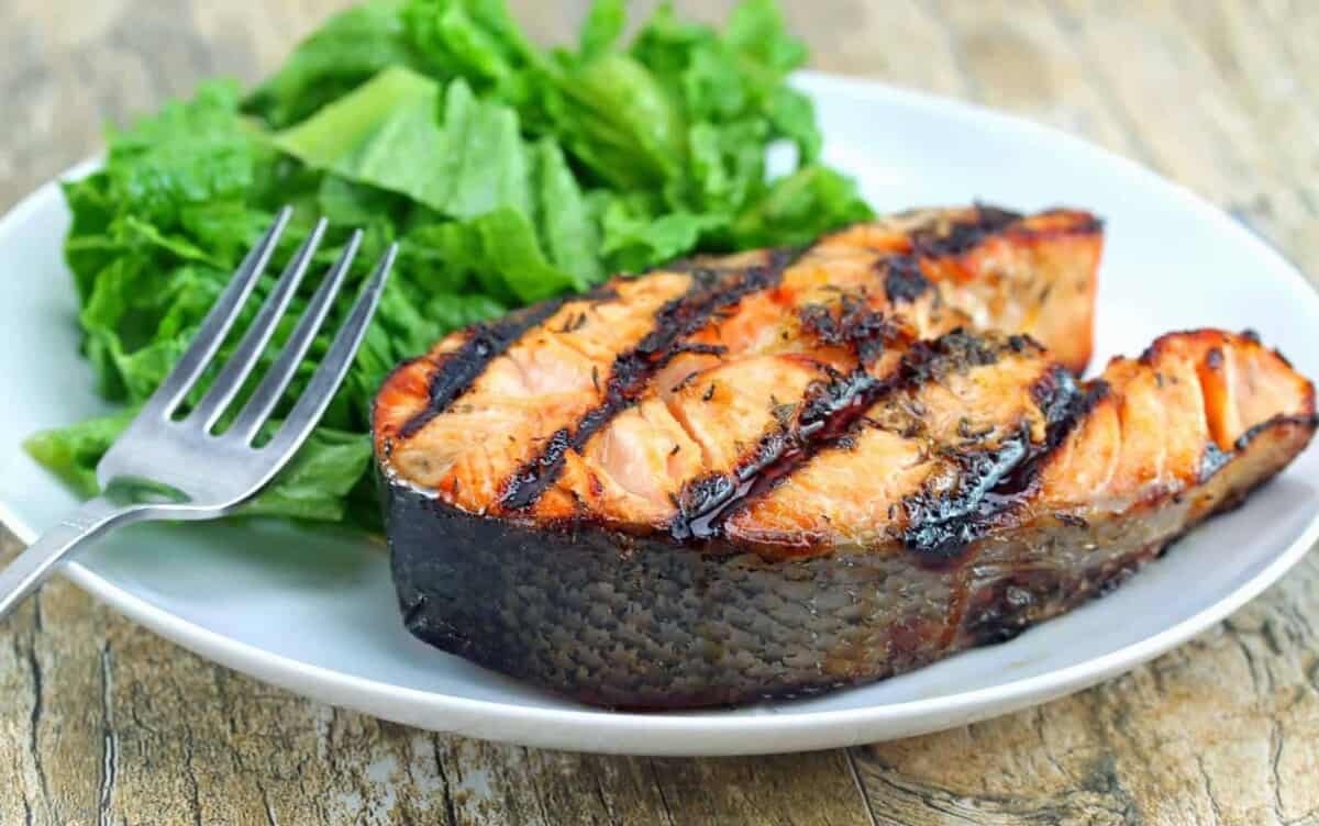 Orange-Ginger Grilled Salmon Steaks on a white plate with a small salad and a fork.