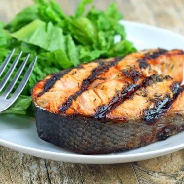Orange-Ginger Grilled Salmon Steaks on a white plate with a small salad and a fork.