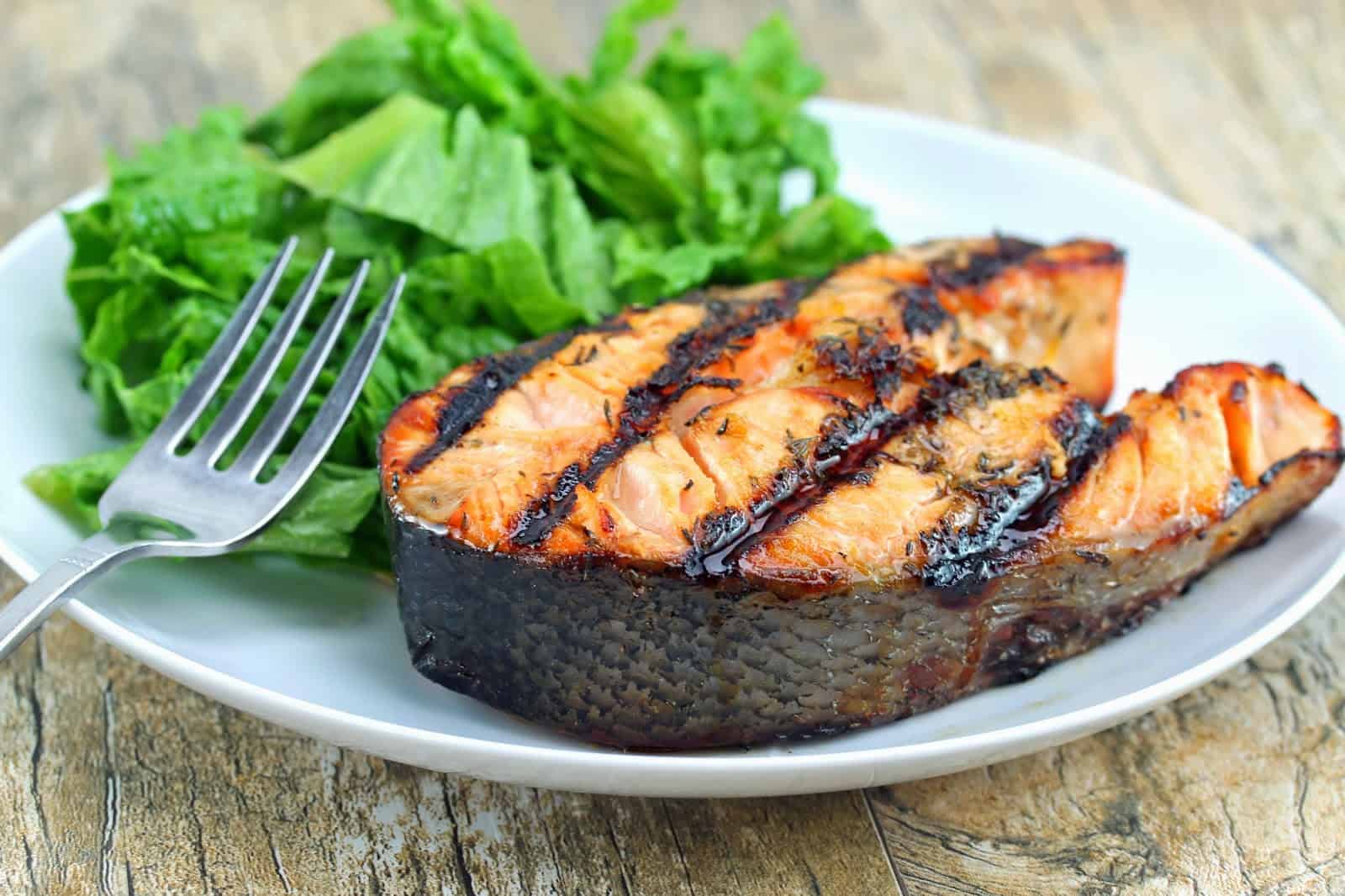 Orange-Ginger Grilled Salmon Steaks on a white plate with a small salad and a fork.