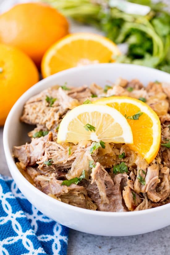 A bowl of Slow Cooker Cuban Mojo Pork garnished with chopped fresh cilantro and orange slices