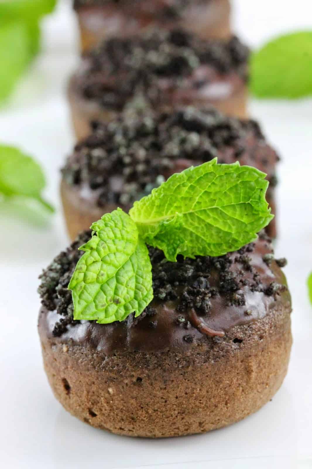 Three Baked chocolate donuts with mint frosting with the first one being topped with mint leaves.