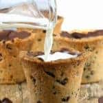 Milk is poured into a cookie shaped into a shot glass that is lined with milk chocolate. Chocolate chips scattered in foreground