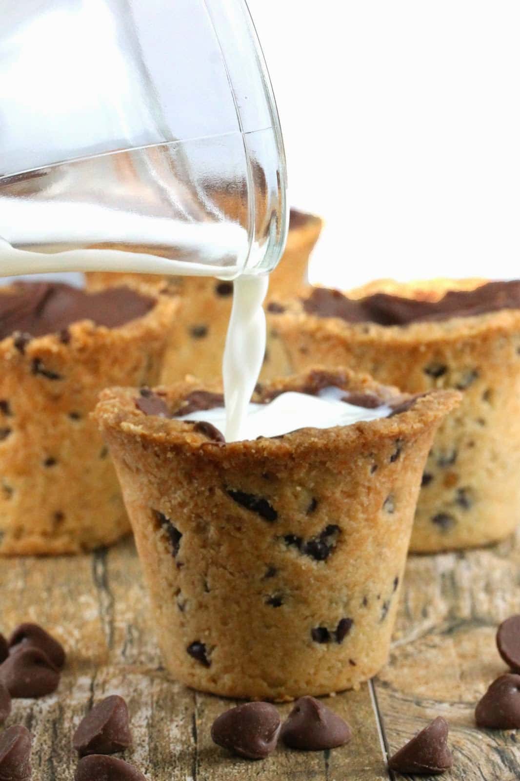 Milk is poured into a cookie shaped into a shot glass that is lined with milk chocolate. Chocolate chips scattered in foreground