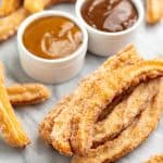 Angled view of Churros on a countertop with a bowl of caramel sauce and a bowl of chocolate sauce.