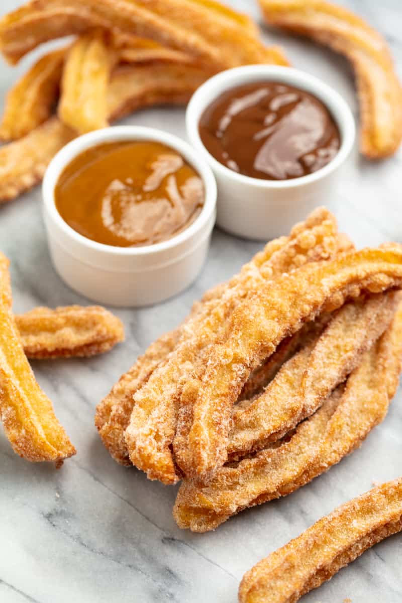 Angled view of Churros on a countertop with a bowl of caramel sauce and a bowl of chocolate sauce.