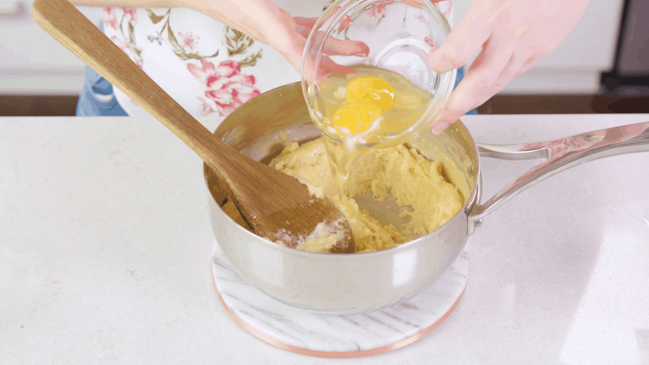 An egg being poured from a bowl into a saucepan filled with churro dough