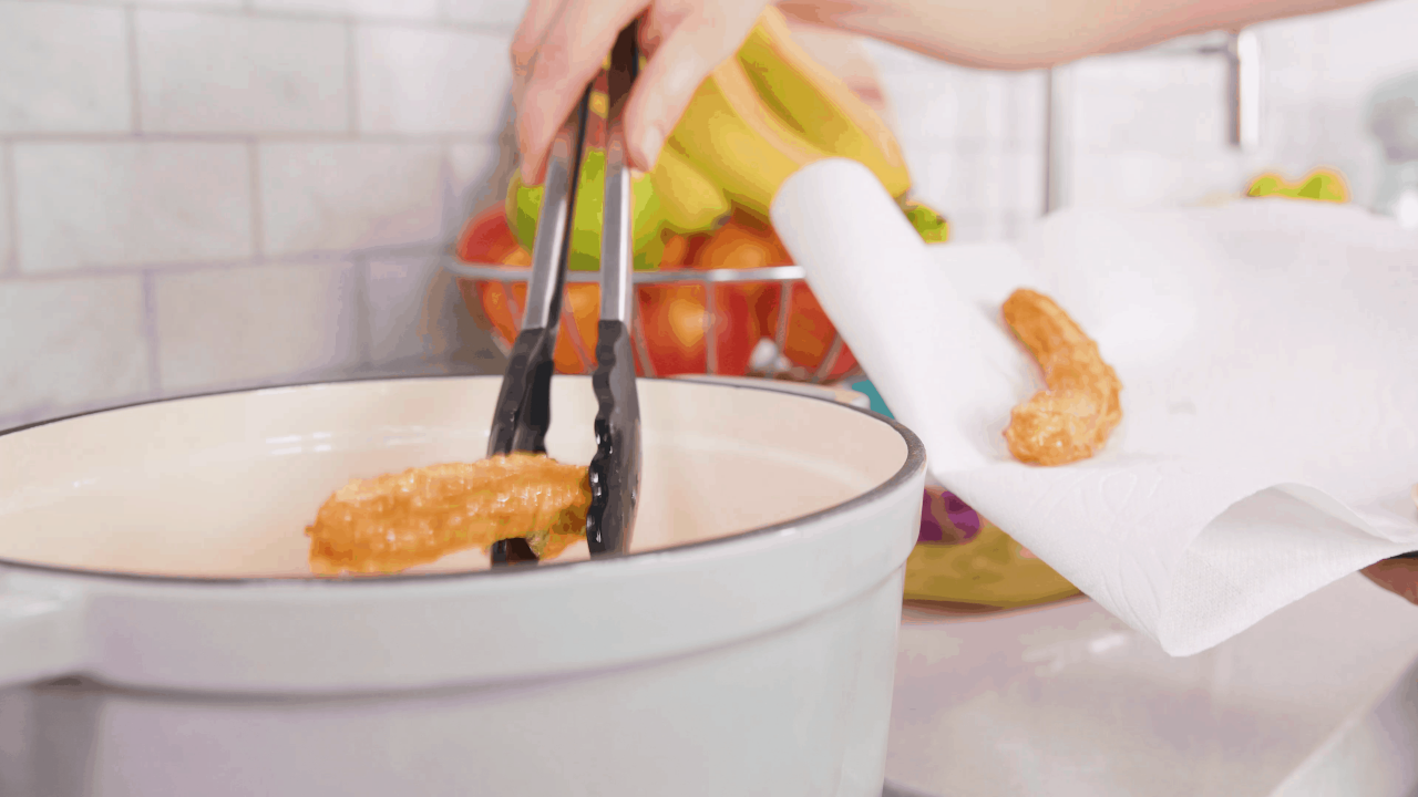 Cooked churro being removed from hot oil using tongs