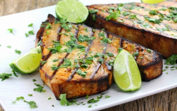 Cilantro-Lime Grilled Swordfish topped with parsley and lime wedges on a white plate.