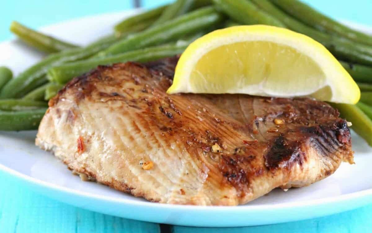 Grilled Thresher Shark topped with a lemon wedge on a white plate with green beans.