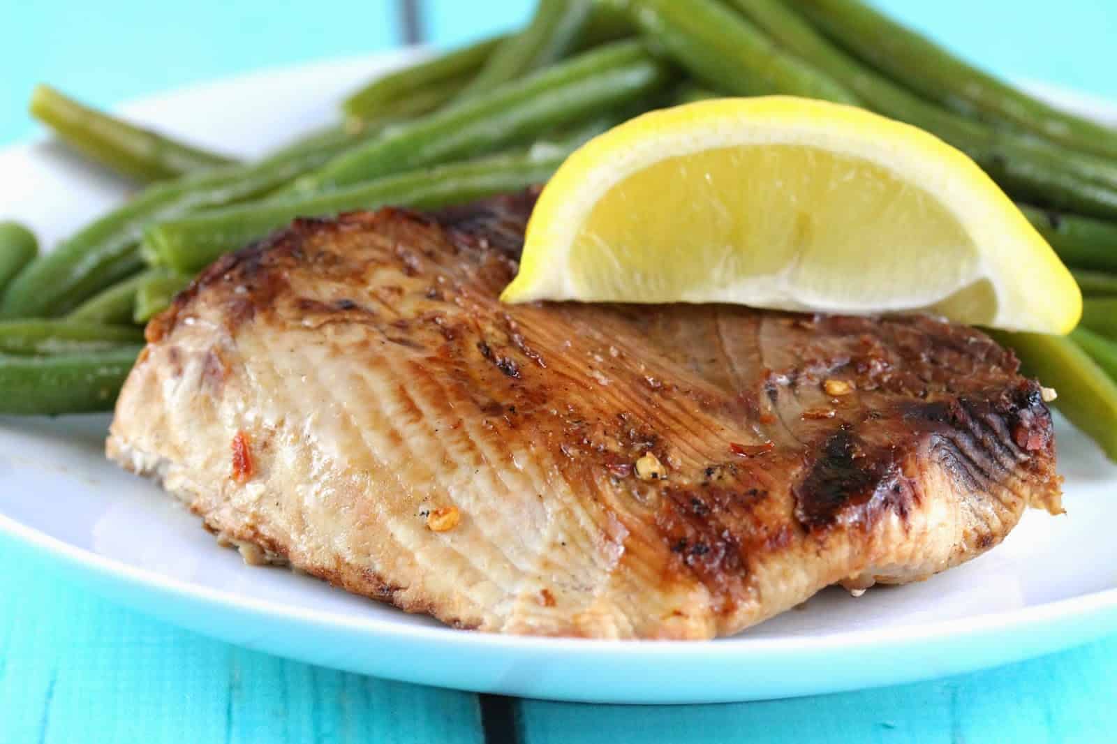 Grilled Thresher Shark topped with a lemon wedge on a white plate with green beans.