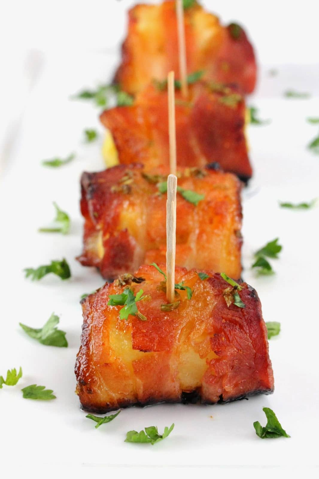 A line of 4 Sriracha Honey Glazed Bacon Wrapped Pineapples stuck together toothpicks