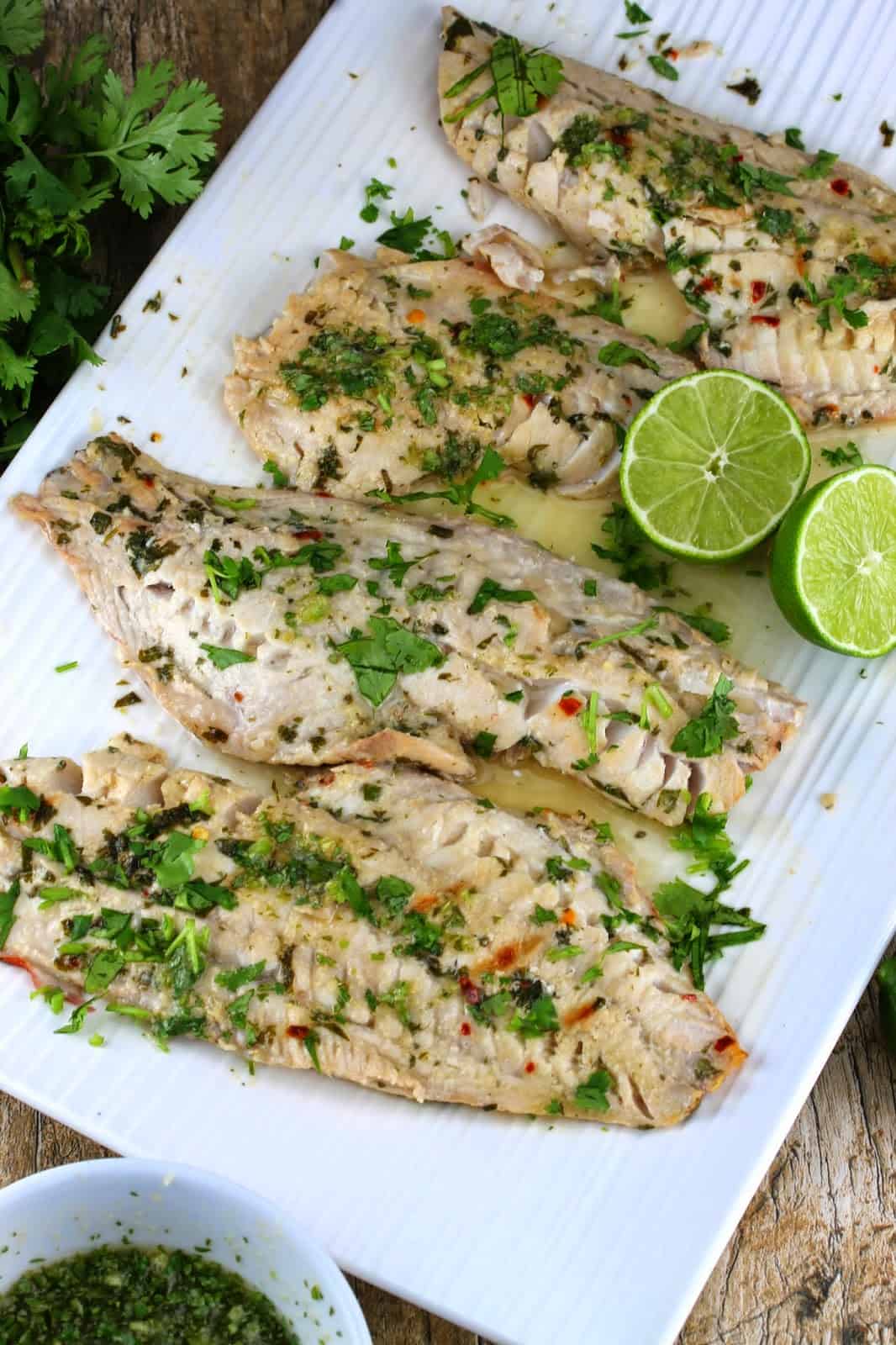 Thai grilled fish with lime wedges on a white serving platter