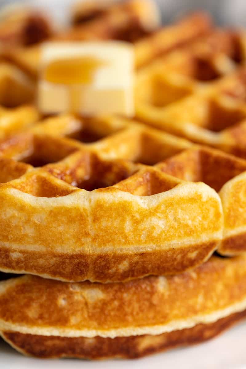 Stack of two waffles with a pad of butter and covered in syrup on a white plate.