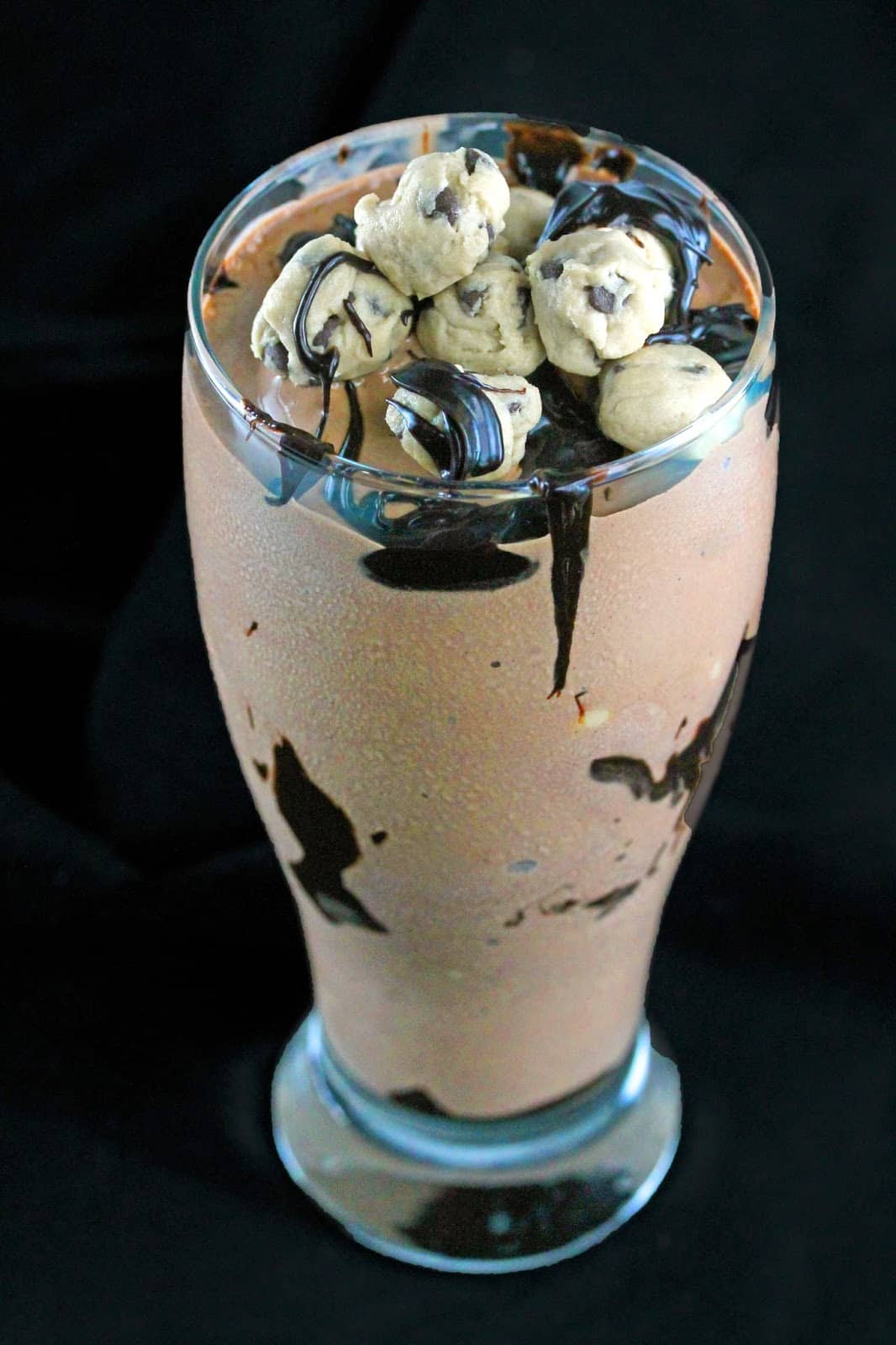 Double Chocolate Fudge Cookie Dough Shake in a large glass topped with cookie dough balls. 