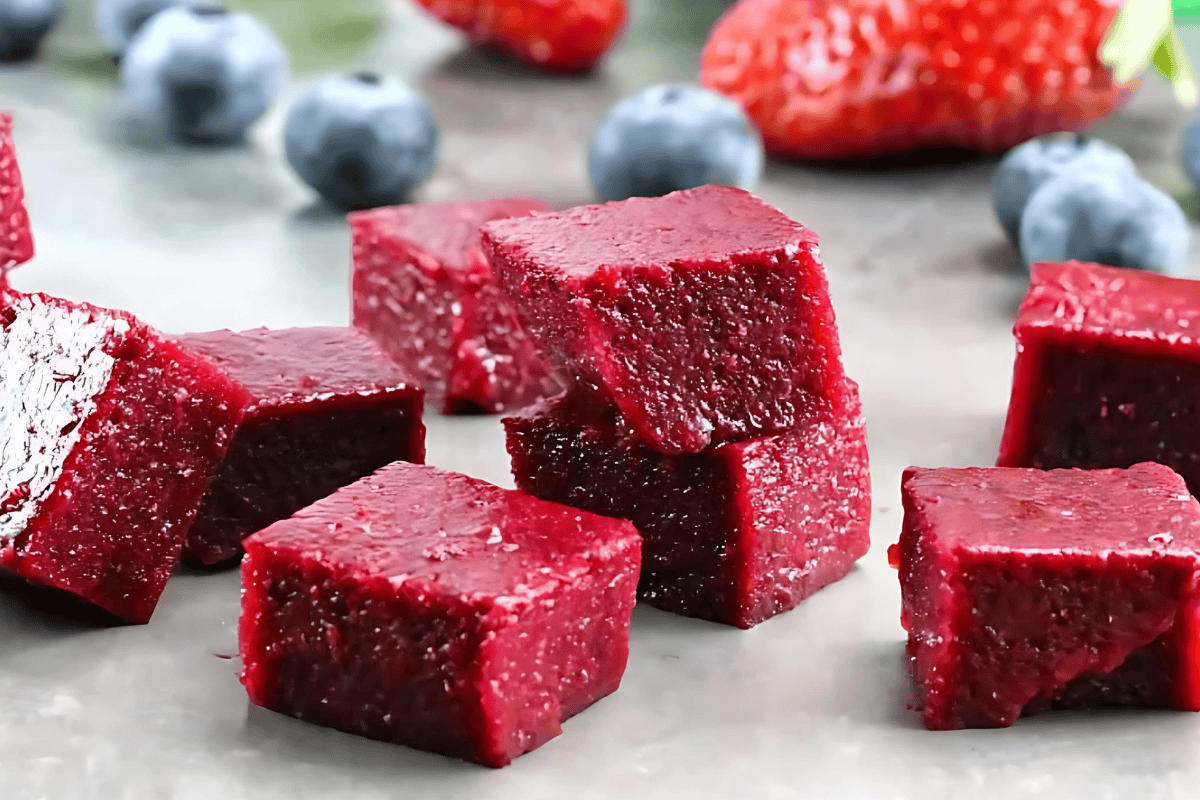 Cubes of Homemade Fruit and Vegetable Snacks stacked on a counter with fresh berries in the background.