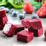 Cubes of Homemade Fruit Snacks stacked on a counter with berries in the background.