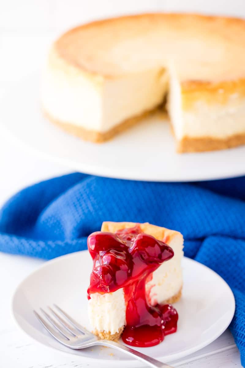 A slice of New York Cheesecake topped a cherry topping with a bite taken out of it on a white plate.