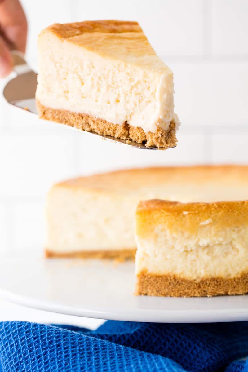 A slice of cheesecake being removed from the full cheesecake.