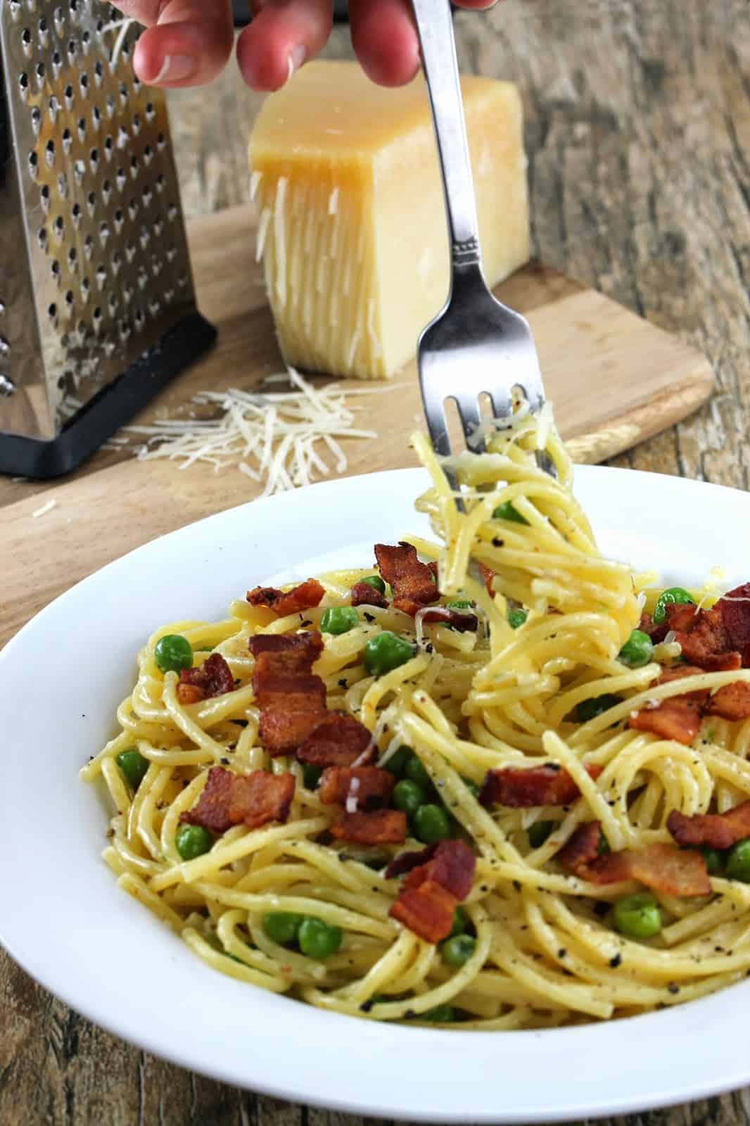 A fork swirls a bite of Quick Bacon and Pea Pasta (Eggless Spaghetti Carbonara) which is topped with crispy bacon and peas