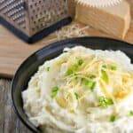 A bowl of smoked gouda mashed potatoes garnished with chives and shredded gouda cheese.