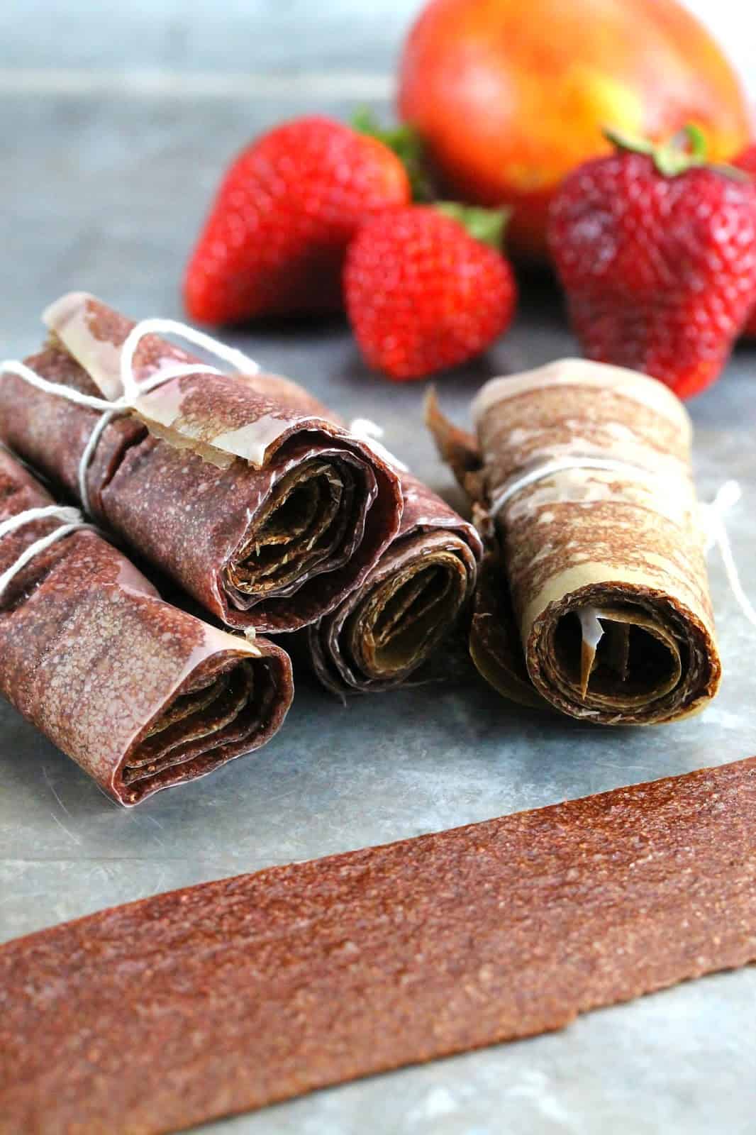 A stack of No Simmer Strawberry-Nectarine Fruit Roll Ups rolled in parchment paper and tied with a string