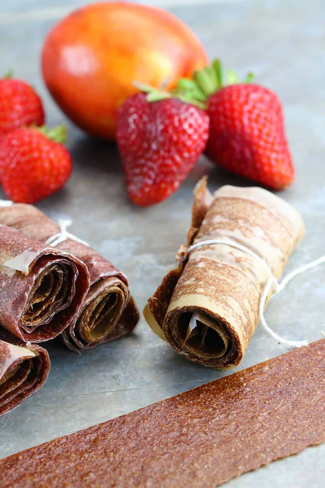 A stack of No Simmer Strawberry-Nectarine Fruit Roll Ups rolled in parchment paper and tied with a string