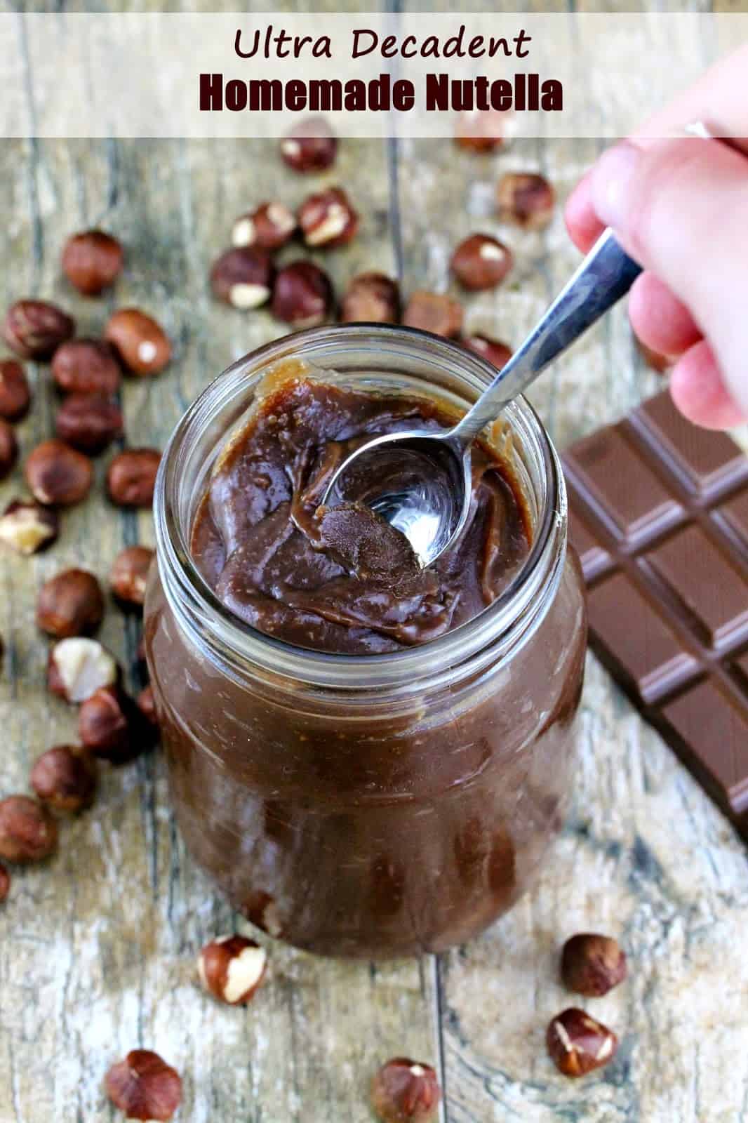 Ultra Decadent Homemade Nutella: A spoonful of creamy homemade Nutella is lifted from a mason jar. Nutella can easily be made at home with chocolate and hazelnuts and a few other simple ingredients. 