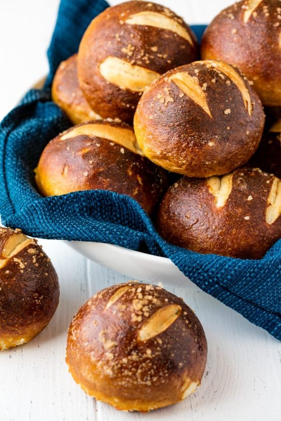 Pretzel Rolls on a white countertop and in a bowl lined with a blue towel.