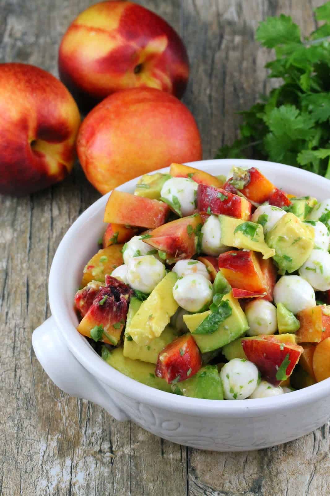 Nectarine and Avocado Fruit Salad in a white bowl sitting next to three nectarines.
