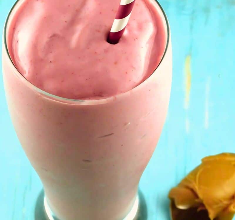 A pink peanut butter and jelly smoothie with a spoon of peanut butter laying next to it.