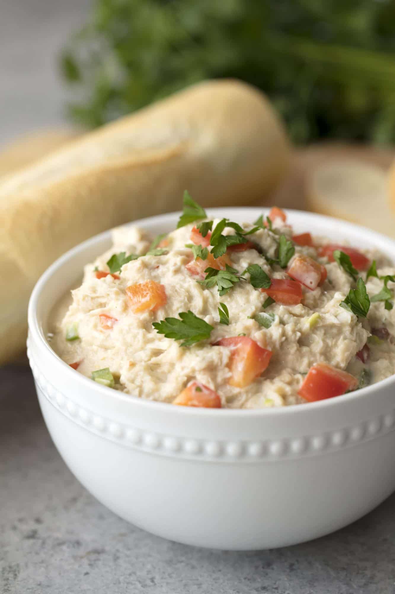 Spicy Crab Dip in a white bowl with bread behind it. 