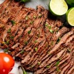 Bird's eye view of Carne Asada surrounded by limes, tomatoes, and jalapenos.