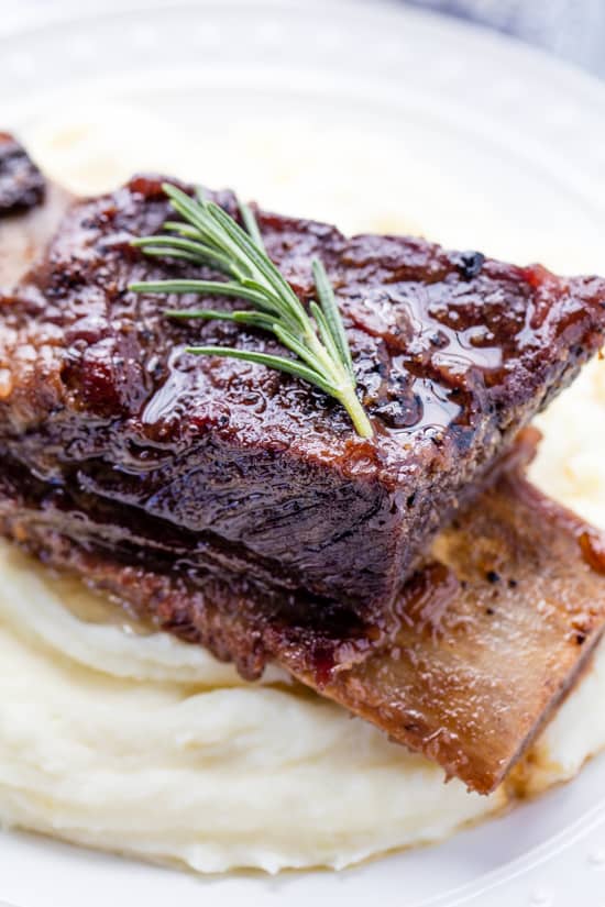 Braised Beef Short Ribs served over mashed potatoes and garnished with a sprig of rosemary