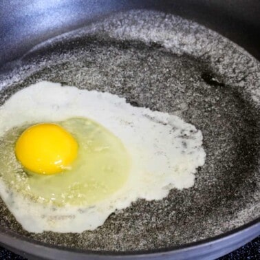 An egg being fried in butter in a skillet.