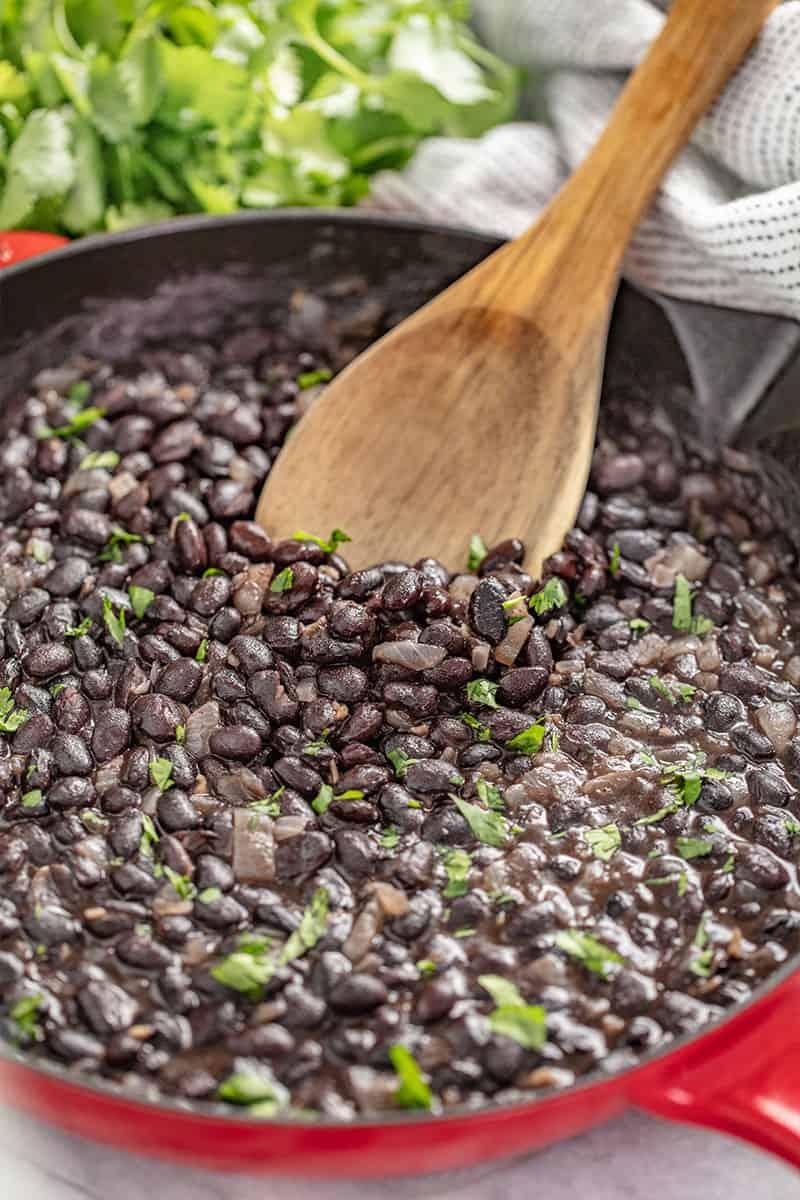 Mexican Black Beans in a cast-iron skillet with a wooden spoon in it. 